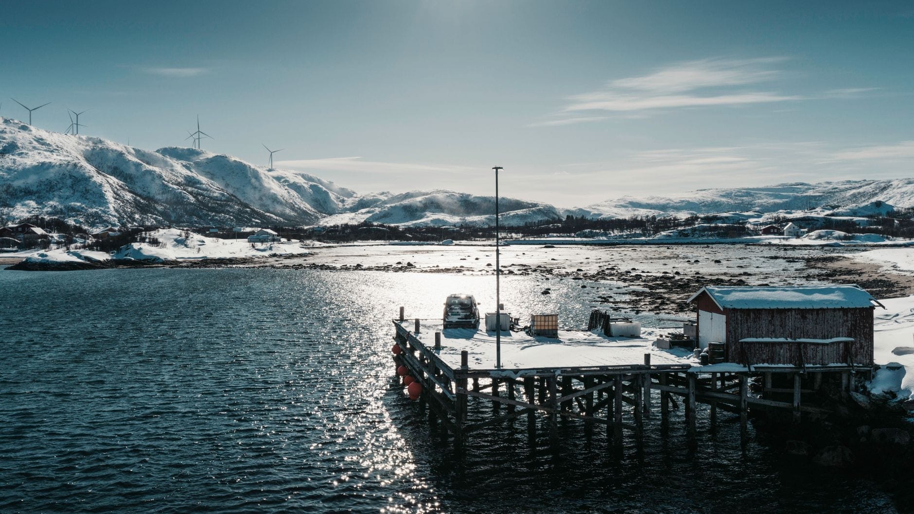En stille trebrygge ved en arktisk fjord med snødekte fjell bak