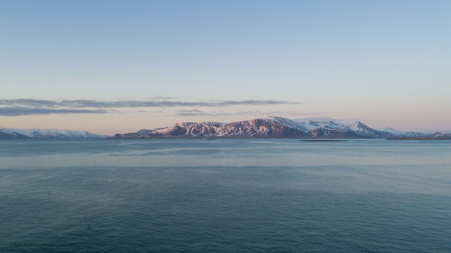 Stille arktisk hav med et fjernt snødekt fjell under en blek himmel