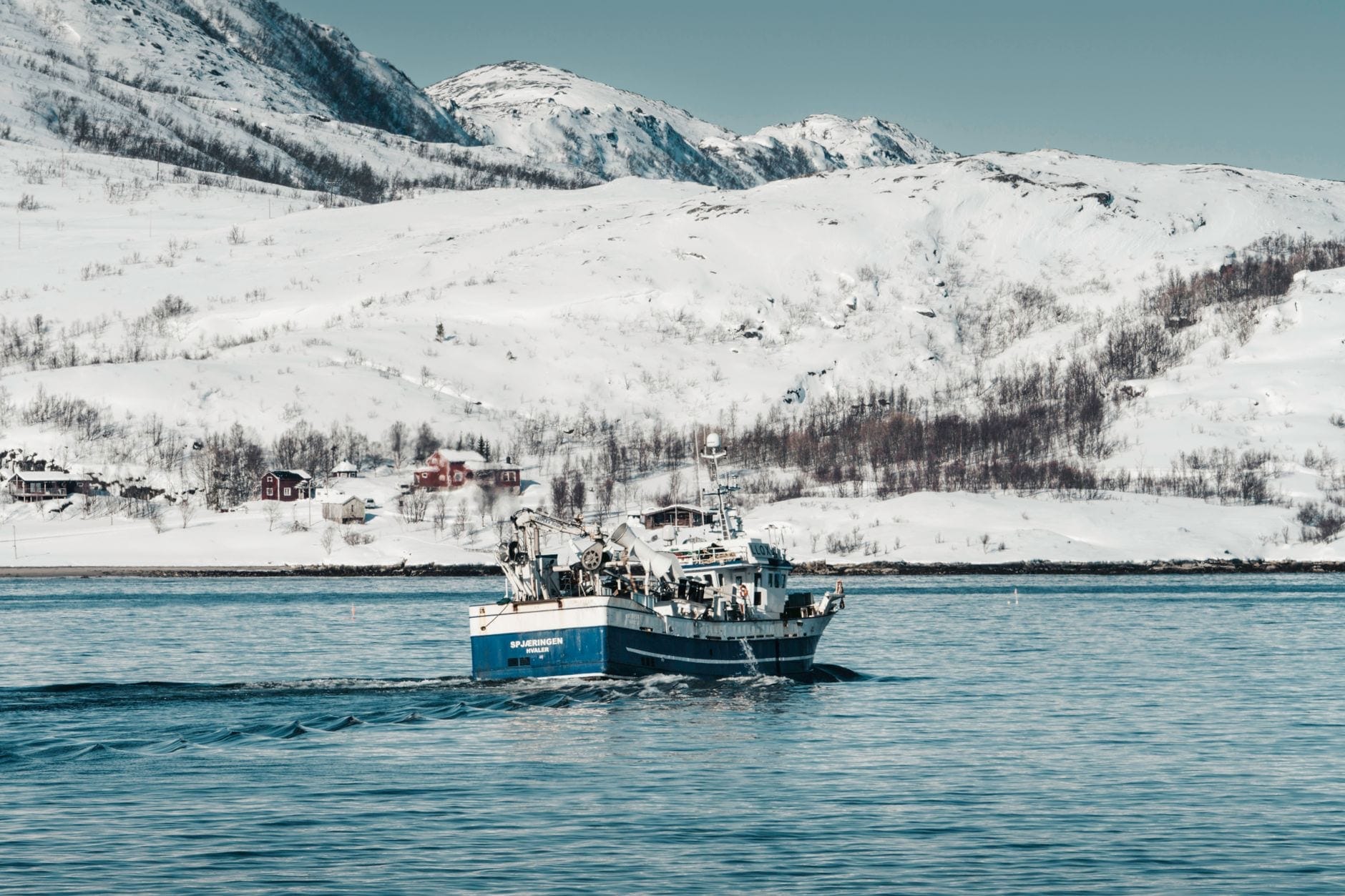En liten fiskebåt som krysser en snødekt norsk fjord
