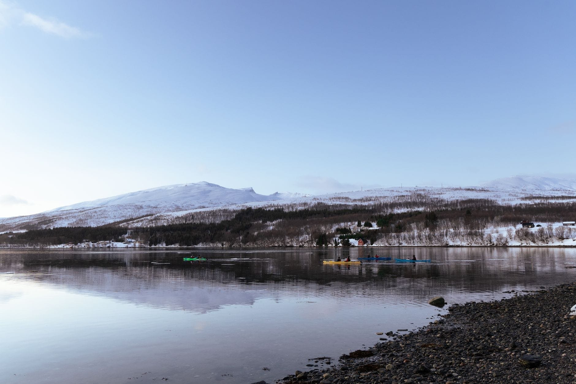 Havkajakker på en snødekt strandlinje ved stille, speilblankt arktisk vann