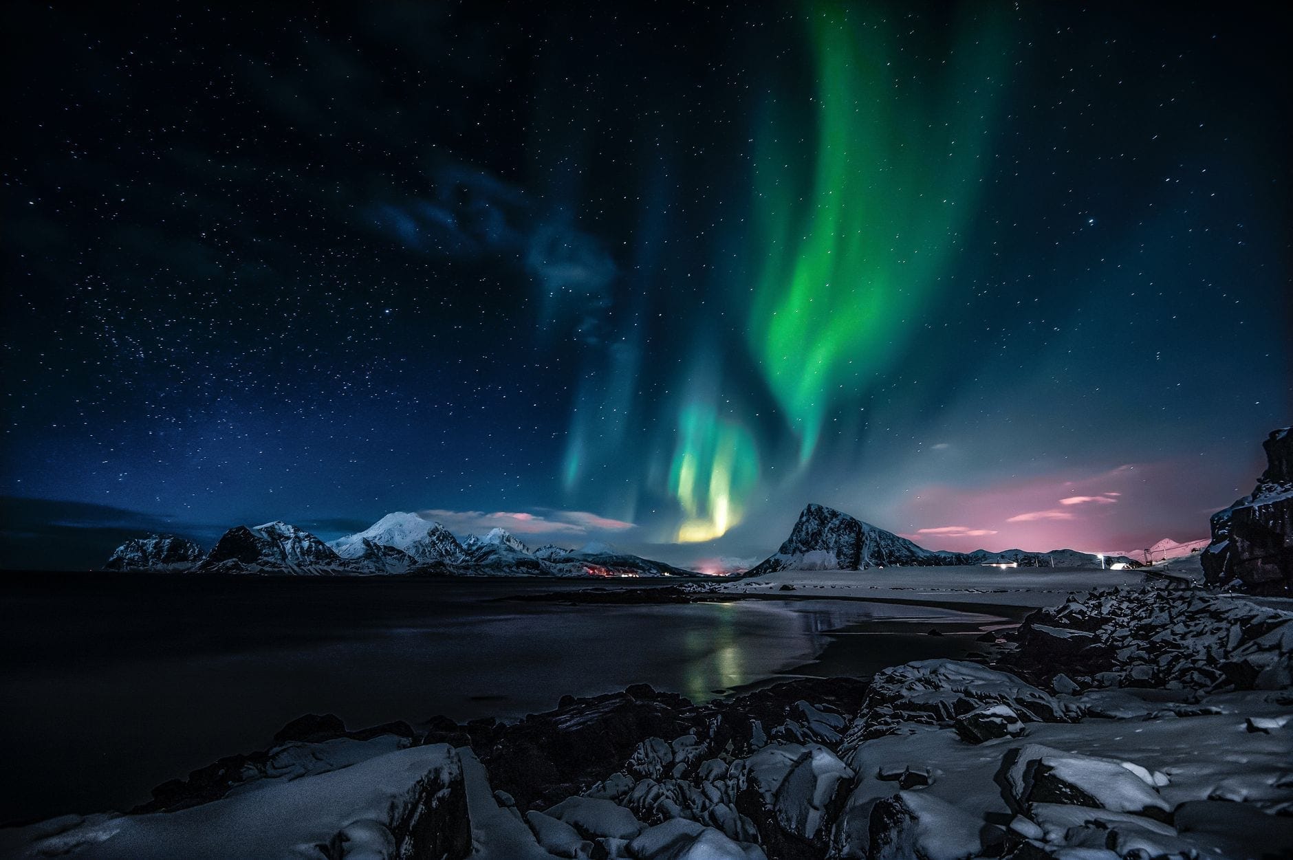 Grønt nordlys over snødekte fjell, speilet i stille fjordvann