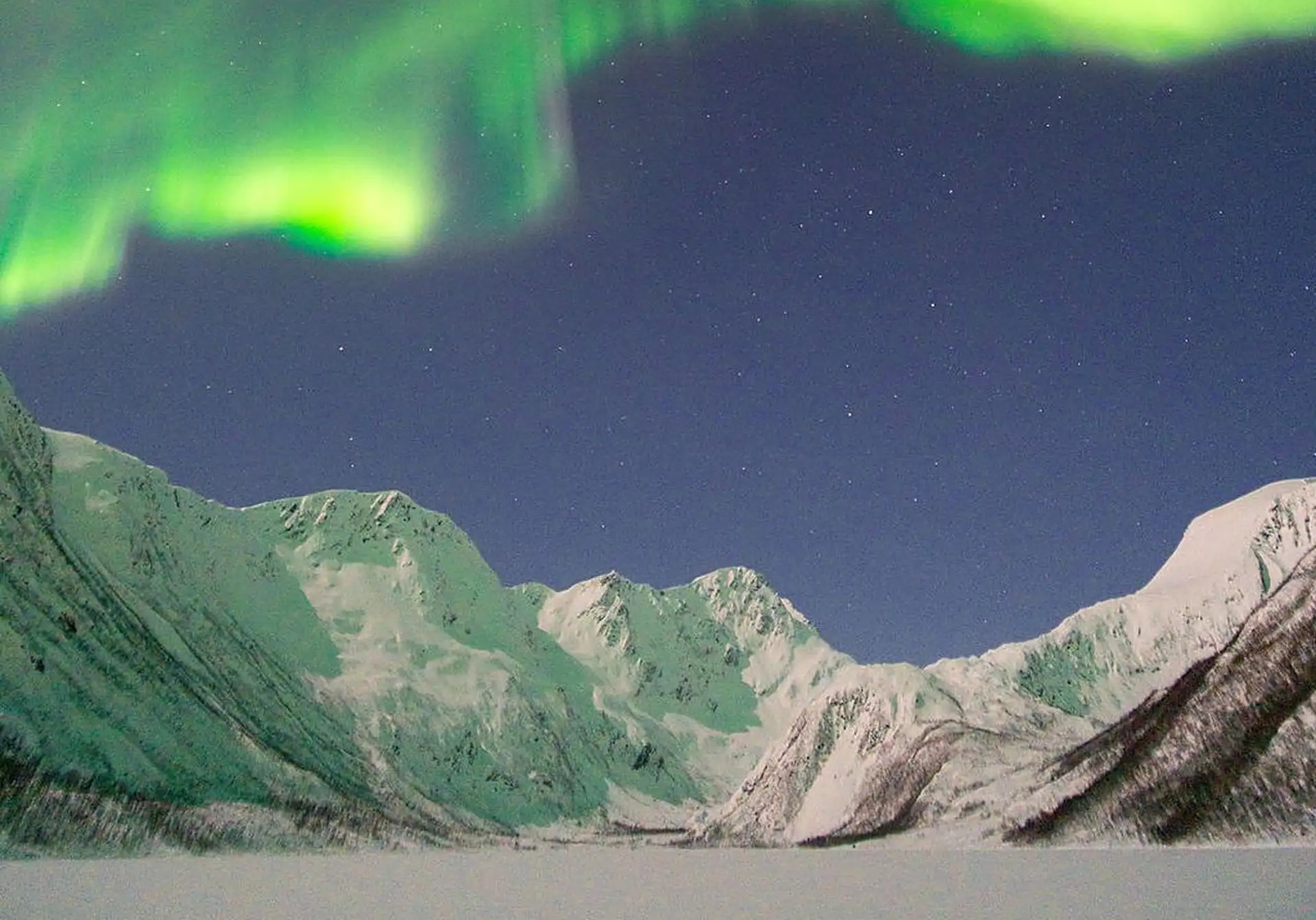 Nordlys over de snødekte fjordfjellene sett fra Kvaløya
