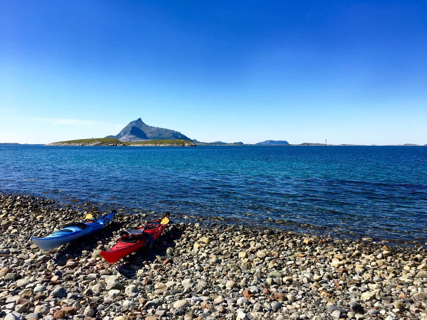 To havkajakker trukket opp på en steinstrand ved klart, kaldt vann